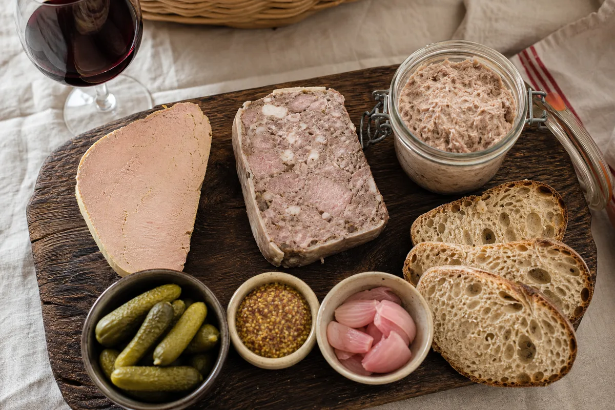 Planche de dégustation réunissant tranche de pâté, part de terrine et pot de rillettes avec cornichons, moutarde et pain de campagne